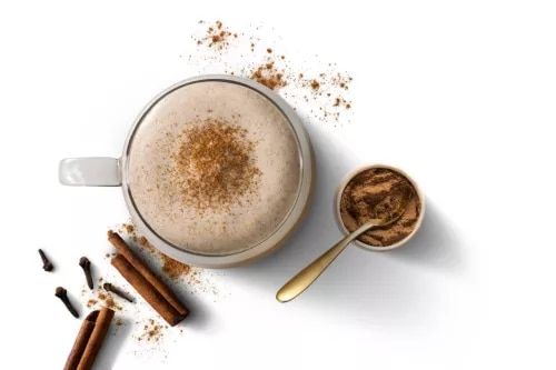 Fotografía cenital de cappuccino con espuma y canela, cuchara dorada y palitos de canela