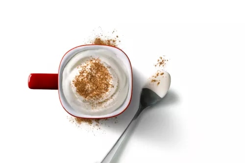 Fotografía cenital de taza roja con café espumoso y canela, cucharilla al lado