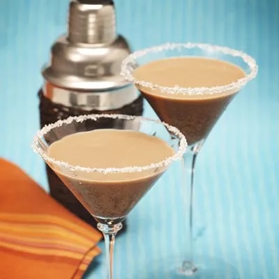 Photo: two sugar-rimmed martini glasses with creamy chocolate cocktails on blue background