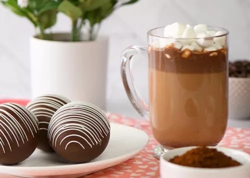 Photograph: glass mug of hot chocolate with marshmallows; two chocolate truffles on white plate