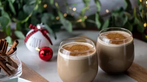 Fotografía de dos cafés con espuma y canela, adornos navideños y palitos.
