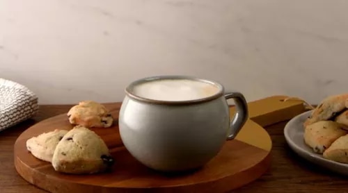 Photo: gray mug of frothy coffee on wooden board with scones and plate in background