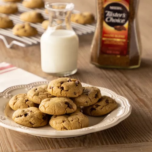 Fotografía: galletas con chispas de chocolate en plato blanco, jarra de leche y frasco