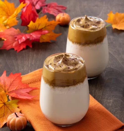 Photograph: two layered whipped coffees on orange napkin with autumn leaves and mini pumpkins