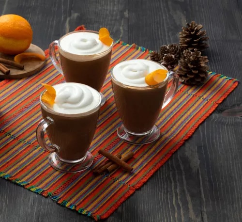 Photo: three glass mugs of hot chocolate with whipped cream and orange peel, pinecones.