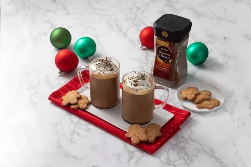 Fotografía: dos tazas de chocolate caliente con crema y galletas sobre bandeja roja, adornos navideños.