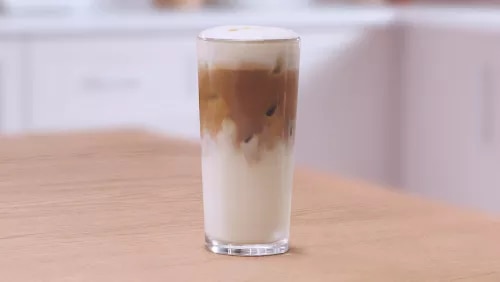 Photograph: tall glass of iced latte with layered milk and espresso on wooden table