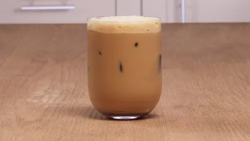 Photograph: short glass of iced coffee with foam and ice on wooden table
