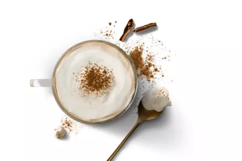 Cappuccino with cinnamon dust, gold spoon with foam, spilled cocoa and two coffee beans