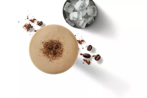 Top-down photo of iced coffee with cocoa dust, glass of ice and scattered coffee beans