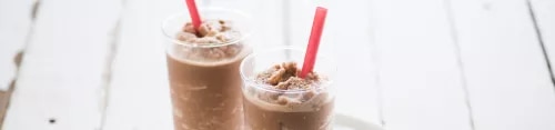 Photograph: two chocolate milkshakes with whipped cream and red straws on white wooden table