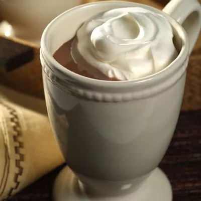 Photograph: white mug of hot chocolate topped with whipped cream on a wooden table.