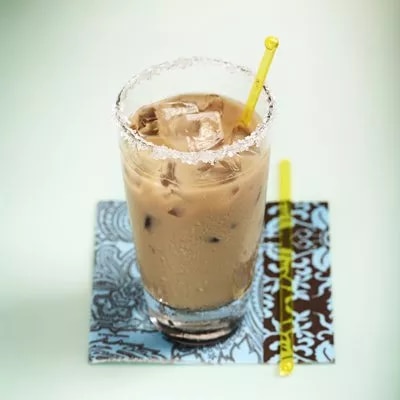 Iced coffee with ice and yellow straw in a rimmed tall glass on blue patterned coaster with second straw beside