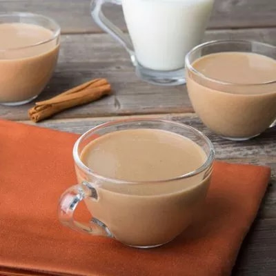 Photograph: three glass cups of milky chai on a wooden table with cinnamon sticks