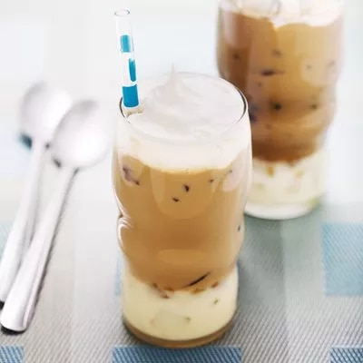 Photograph of two layered iced lattes with milk base, whipped cream topping, blue-striped straw