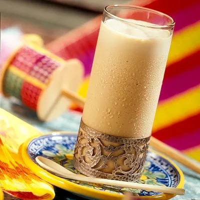 Fotografía de vaso alto con bebida cremosa y condensación sobre plato azul decorado
