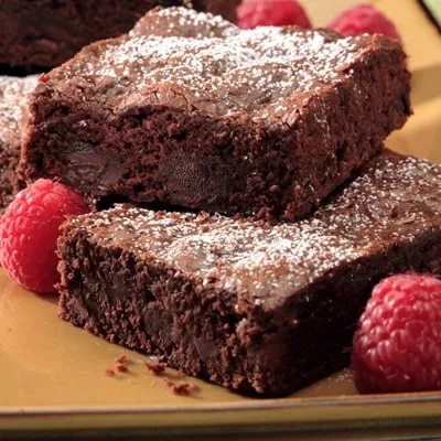 Photograph: two fudgy chocolate brownies dusted with powdered sugar, with raspberries