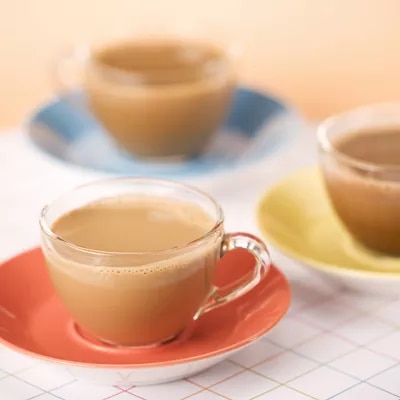 Foto: tres tazas de café con leche en platillos naranja, azul y amarillo sobre mantel cuadriculado