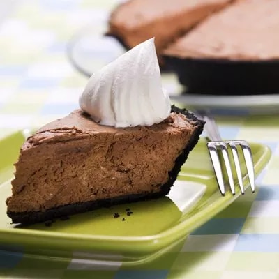 Fotografía de porción de tarta de chocolate con base de galleta y crema batida en plato verde
