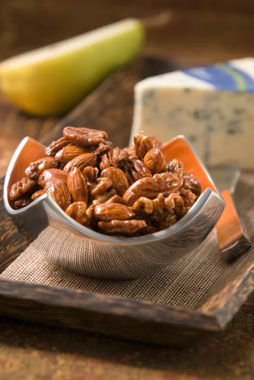 Fotografía de nueces glaseadas en cuenco naranja, queso azul y pera al fondo