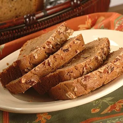 Photo: sliced pecan loaf on white plate over floral tablecloth