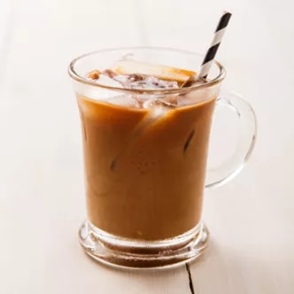 Fotografía de café helado en vaso de vidrio con hielo y pajita sobre mesa clara
