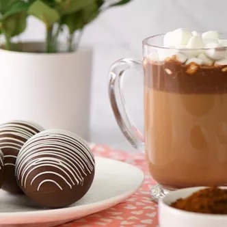 Fotografía: taza de vidrio con chocolate y malvaviscos; tres trufas con glaseado en plato.