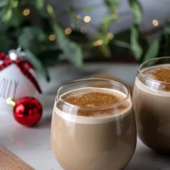 Fotografía de dos cafés con espuma y canela, adornos navideños y palitos.