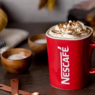 Photograph: red NESCAFÉ mug topped with whipped cream and cinnamon, wooden bowls nearby