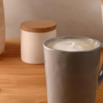 Fotografía: taza gris con café espumoso sobre mesa de madera, tarros blancos al fondo