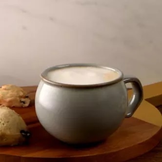 Fotografía: taza gris con café espumoso sobre tabla de madera y bollos pequeños