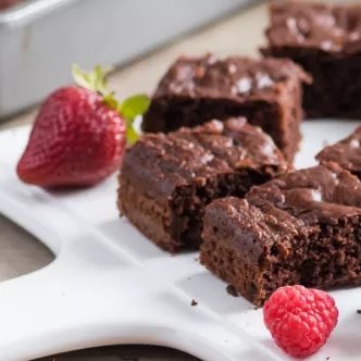 Fotografía de brownies cuadrados con azúcar glas y frambuesas sobre bandeja blanca
