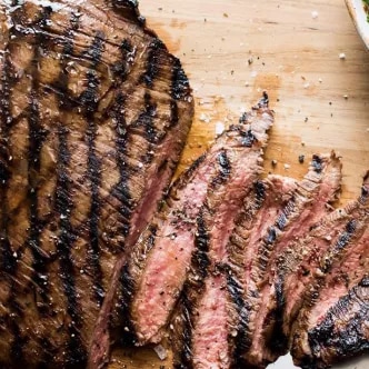 Bistec a la parrilla en tabla de madera, rebanado medio raro con salsa verde al lado