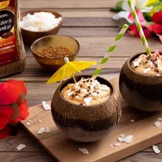 Dos cocos con café cremoso, crema batida, coco rallado, pajillas y flores tropicales