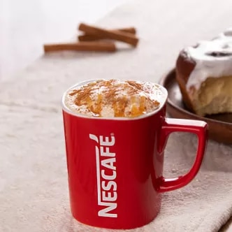 Fotografía: taza roja con logo Nescafé y café espumoso con canela, bollería glaseada