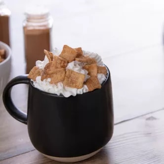 Fotografía: taza negra con chocolate caliente, crema y malvaviscos tostados