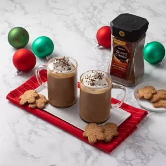 Fotografía: dos tazas de chocolate caliente con crema y galletas sobre bandeja roja, adornos navideños.