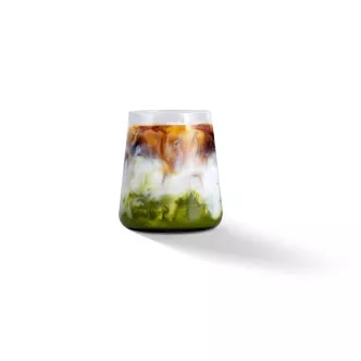 Photograph: low glass with green matcha, white milk and brown coffee swirls on white background
