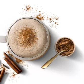 Top-down photograph: frothy cappuccino dusted with cinnamon, spoon of cinnamon, sticks and coffee beans.