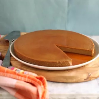 Fotografía de tarta dorada con una porción cortada y base de galleta sobre plato