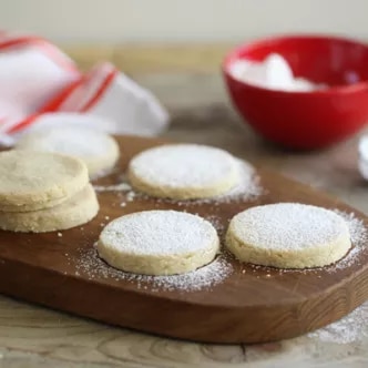 Photograph of round shortbread cookies dusted with powdered sugar on a wooden board