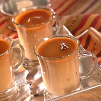 Photograph of three glass mugs with caramel-topped custard and spoons on striped cloth