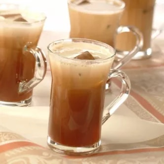 Photograph: three glass mugs of iced coffee topped with creamy foam on a tablecloth
