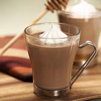 Fotografía: taza de vidrio con chocolate caliente y crema batida sobre mesa de madera