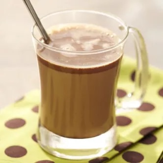 Fotografía: taza de vidrio con chocolate caliente y cuchara sobre servilleta verde con lunares