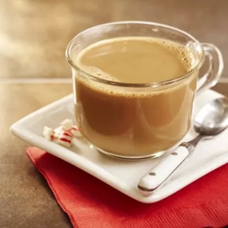 Photograph: glass mug of creamy latte on square saucer with spoon, peppermint and red napkin