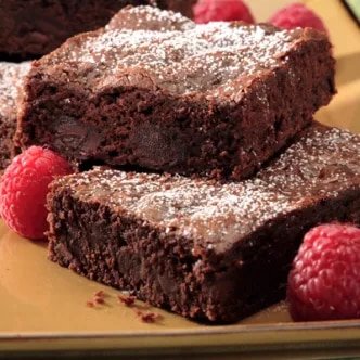 Fotografía: dos brownies de chocolate con azúcar glas, acompañados de frambuesas.