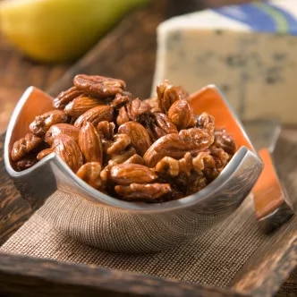 Photograph: glazed pecans in a small bowl on a wooden board with blue cheese wedge and pear slice