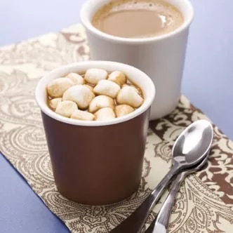 Fotografía de dos tazas: una con malvaviscos sobre chocolate caliente y otra con café, con cucharilla.