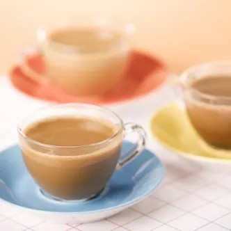 Fotografía de tazas de vidrio con café con leche sobre platos pastel azul, naranja y amarillo